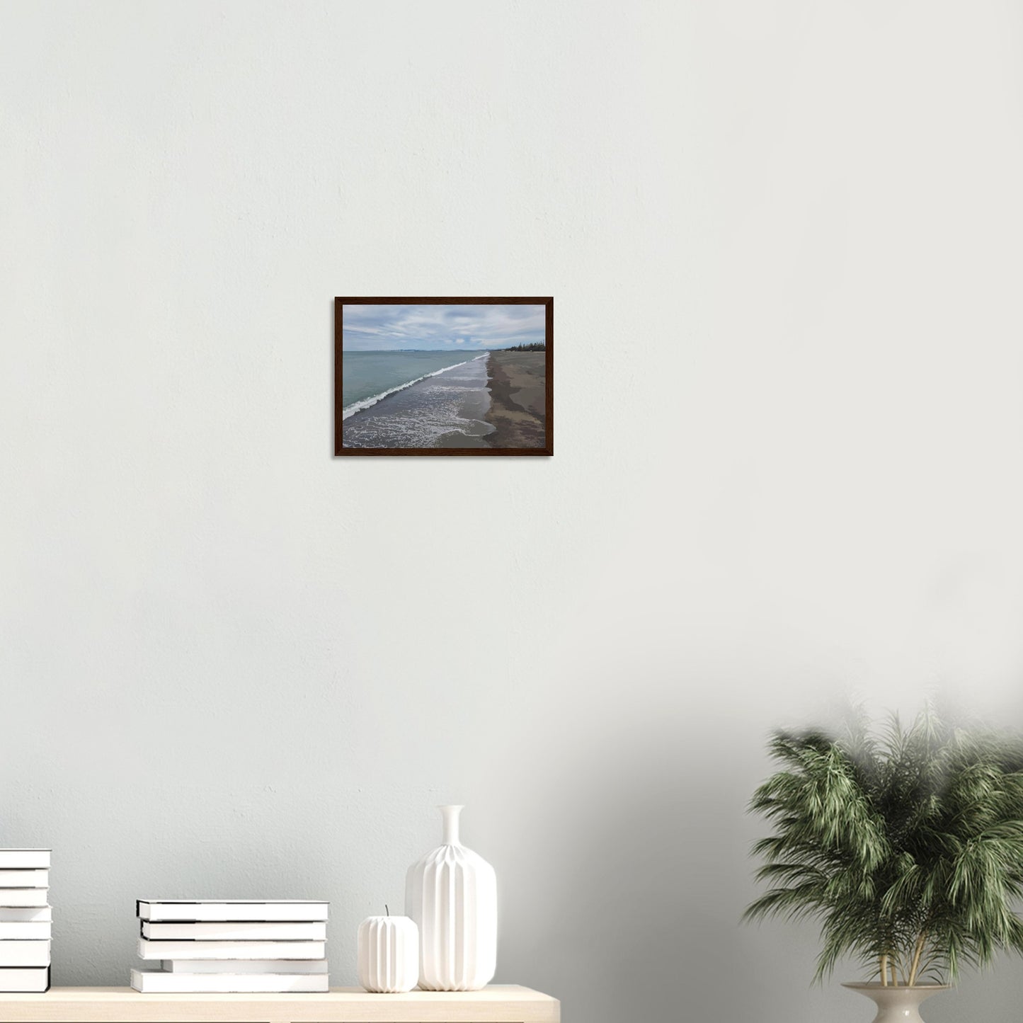 Gentle waves roll onto the dark sand, stretching endlessly into the distance under a softly clouded sky. Hints of pine trees and distant land complete the scene