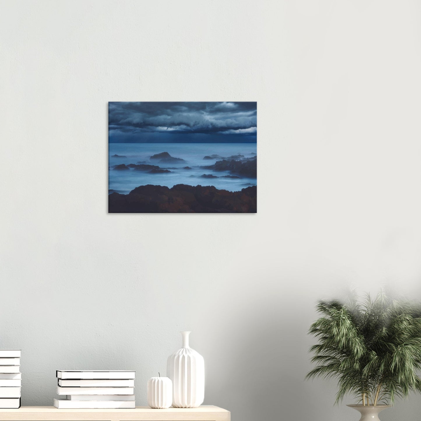 Deep navy and steel-blue tones sweep across a moody sky, while waves crash and swirl around jagged rocks, softened by a misty, dreamlike haze.