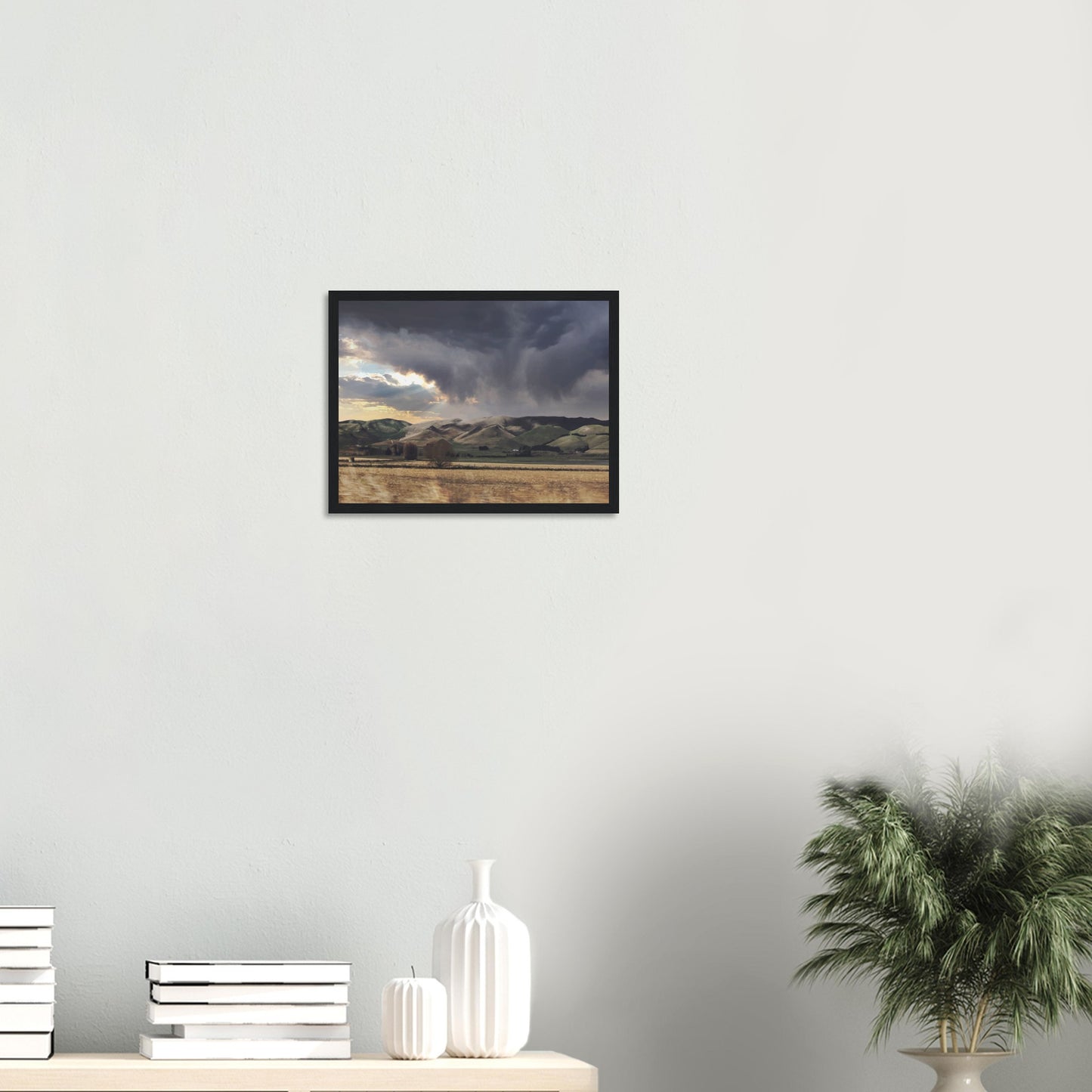 Landscape artwork of Te Hauke hills under dark clouds with beams of light breaking through.