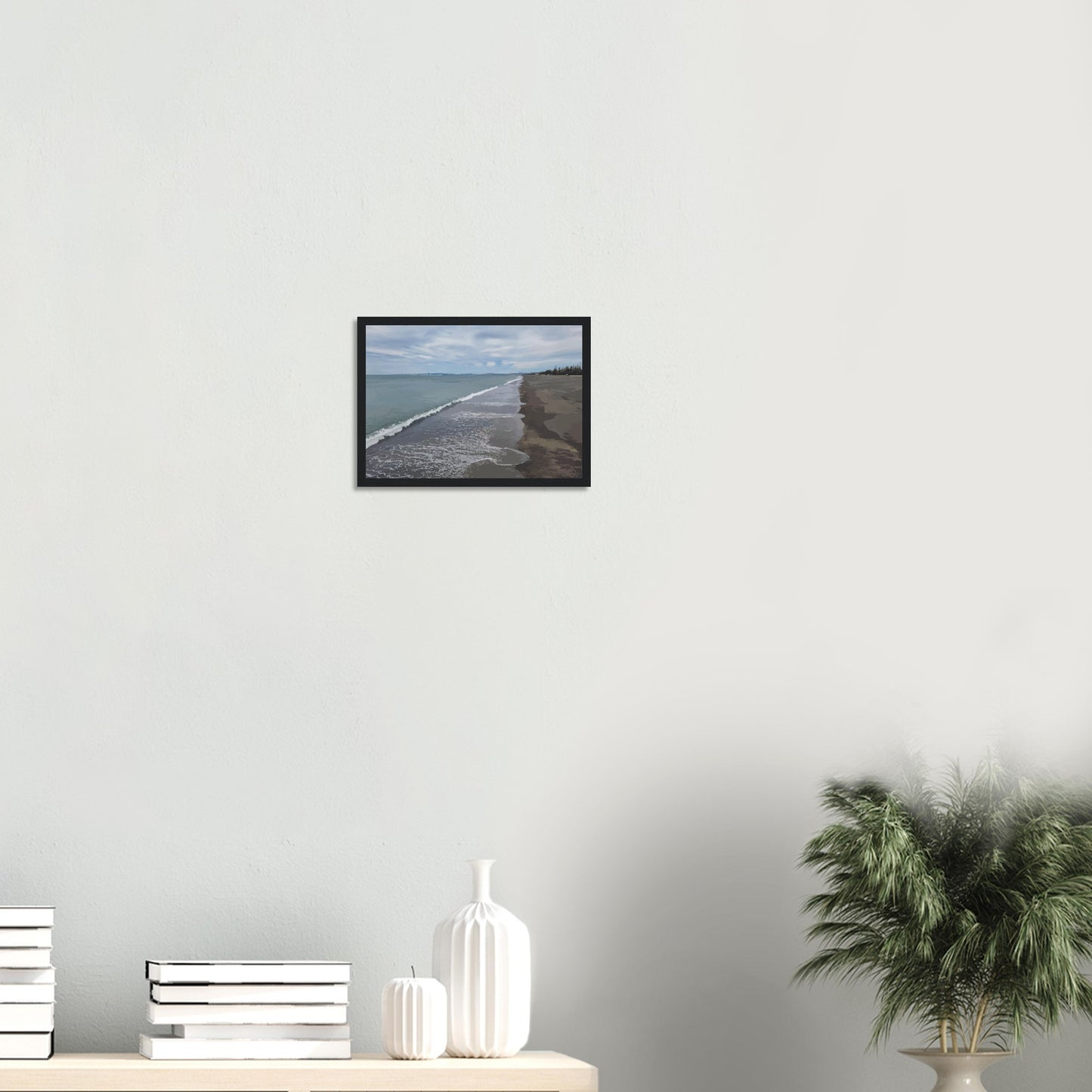 Gentle waves roll onto the dark sand, stretching endlessly into the distance under a softly clouded sky. Hints of pine trees and distant land complete the scene