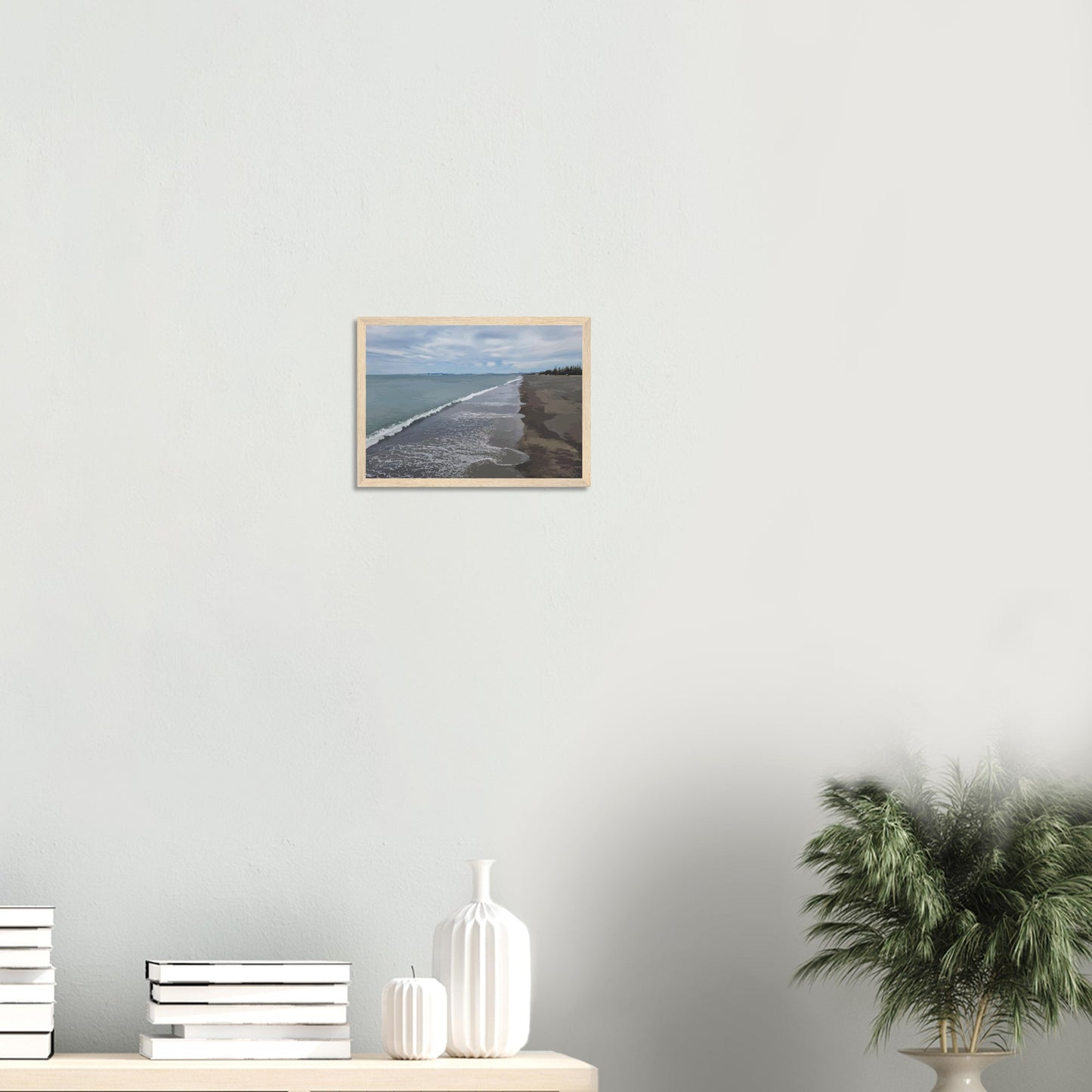 Gentle waves roll onto the dark sand, stretching endlessly into the distance under a softly clouded sky. Hints of pine trees and distant land complete the scene