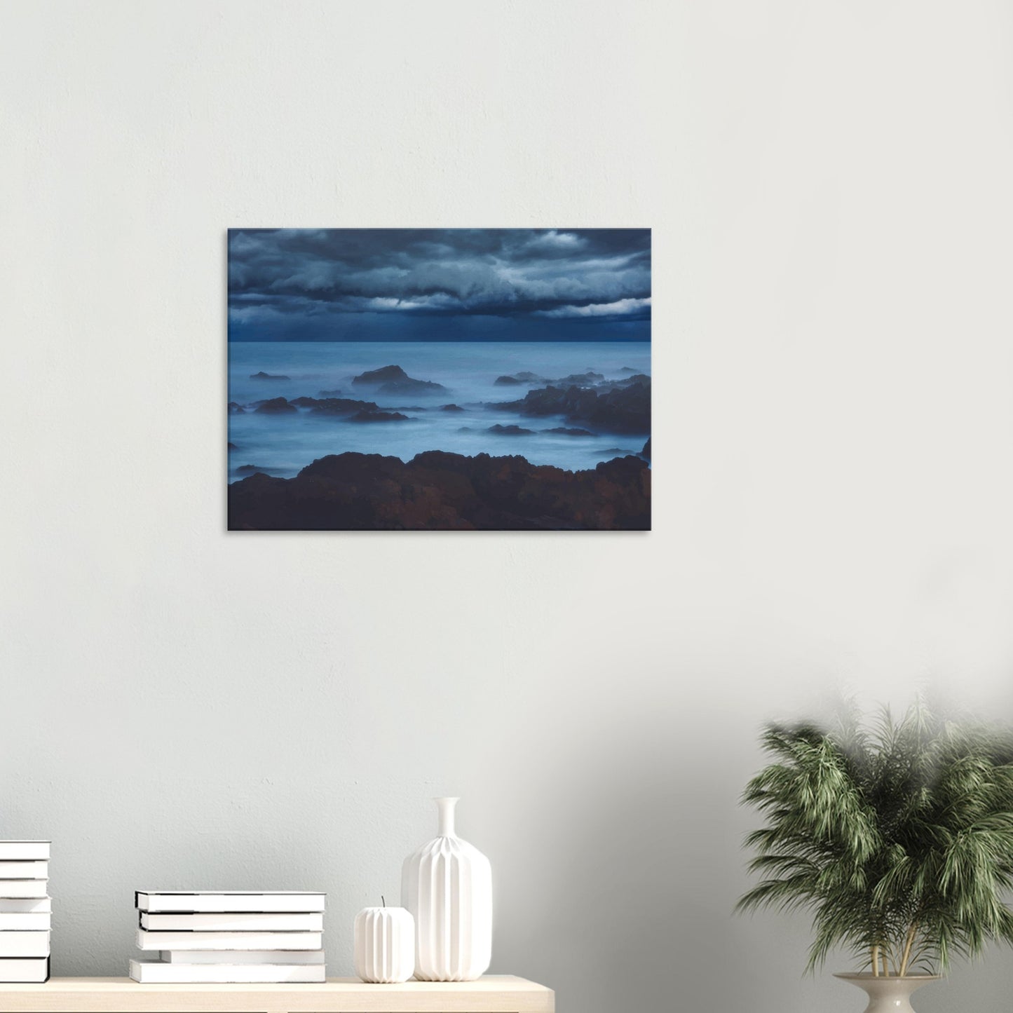Deep navy and steel-blue tones sweep across a moody sky, while waves crash and swirl around jagged rocks, softened by a misty, dreamlike haze.