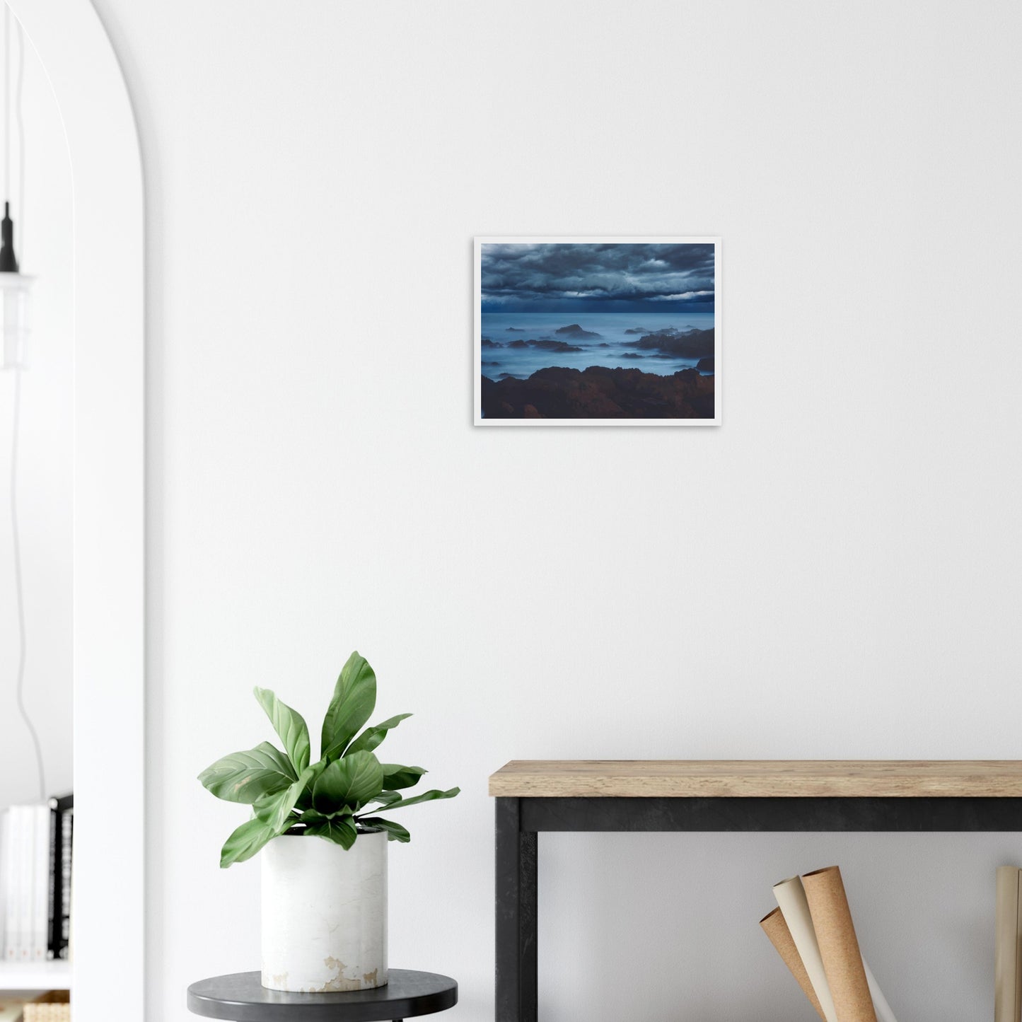 Deep navy and steel-blue tones sweep across a moody sky, while waves crash and swirl around jagged rocks, softened by a misty, dreamlike haze.