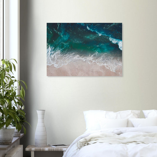 Aerial view of ocean waves rolling onto sand in teal and blue tones.