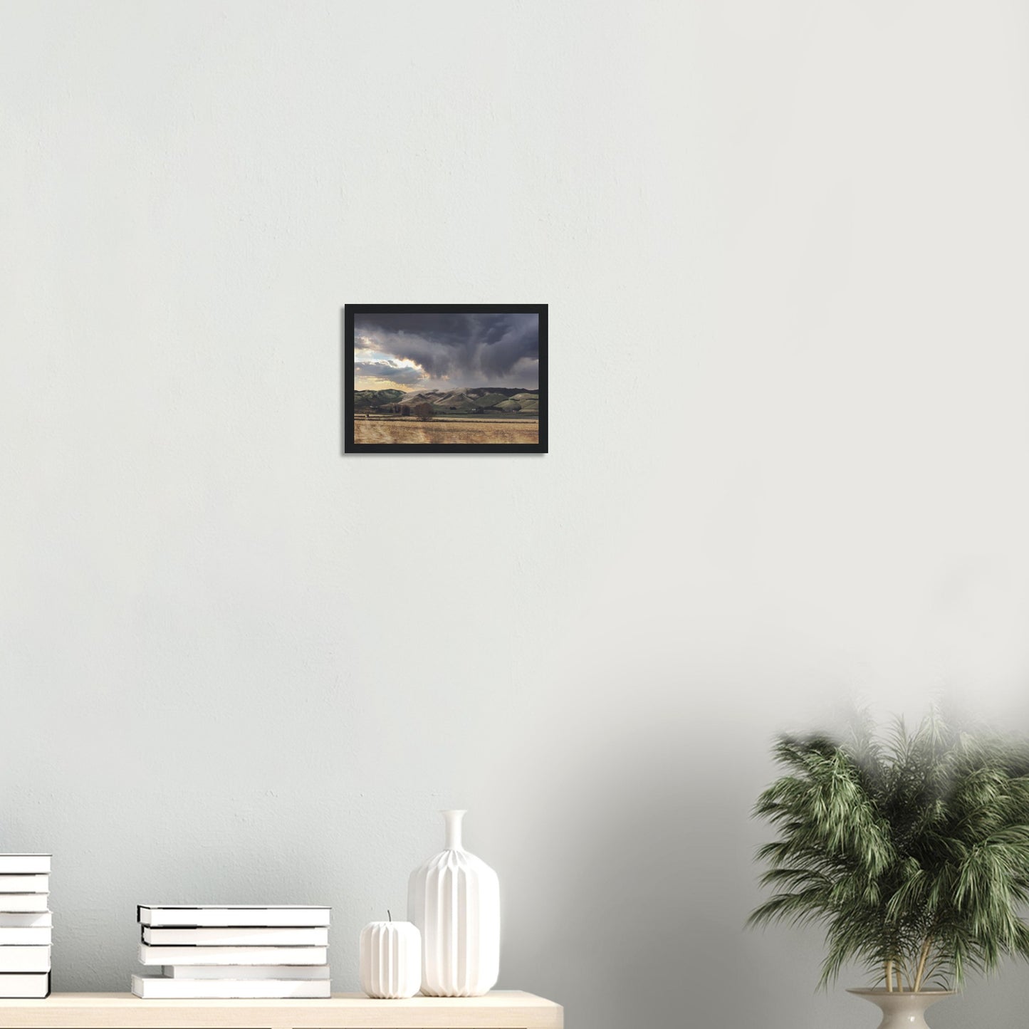 Landscape artwork of Te Hauke hills under dark clouds with beams of light breaking through.