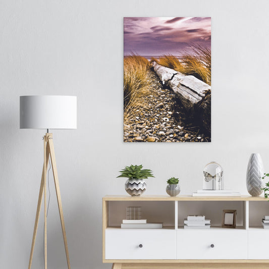 Driftwood lying in coastal grasses under a purple sky, evoking weathered texture and calm.