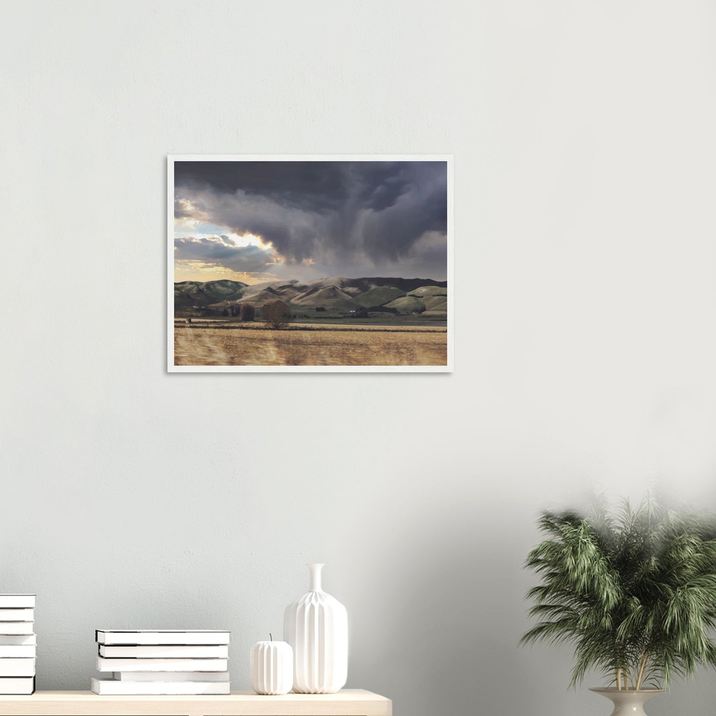 Landscape artwork of Te Hauke hills under dark clouds with beams of light breaking through.