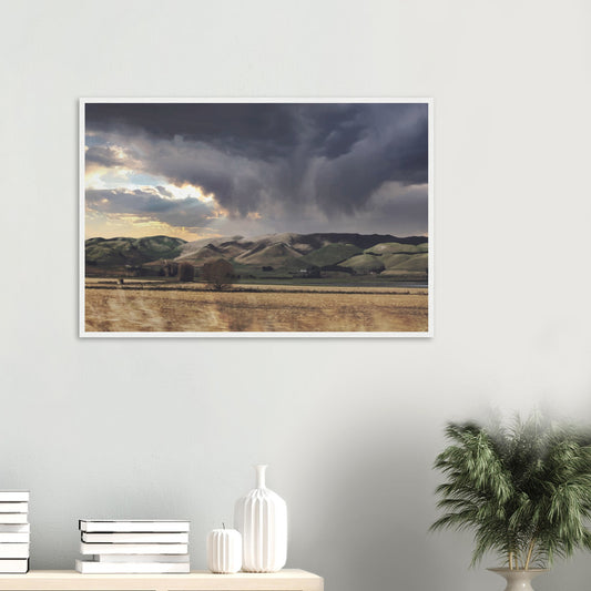 Landscape artwork of Te Hauke hills under dark clouds with beams of light breaking through.