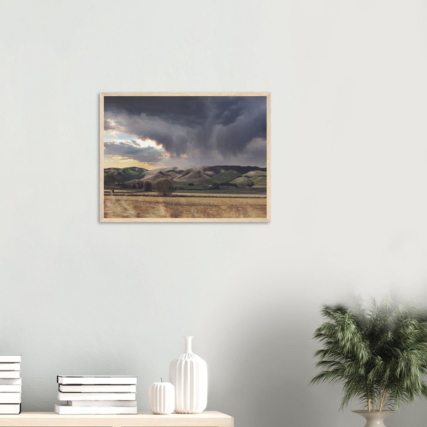 Landscape artwork of Te Hauke hills under dark clouds with beams of light breaking through.