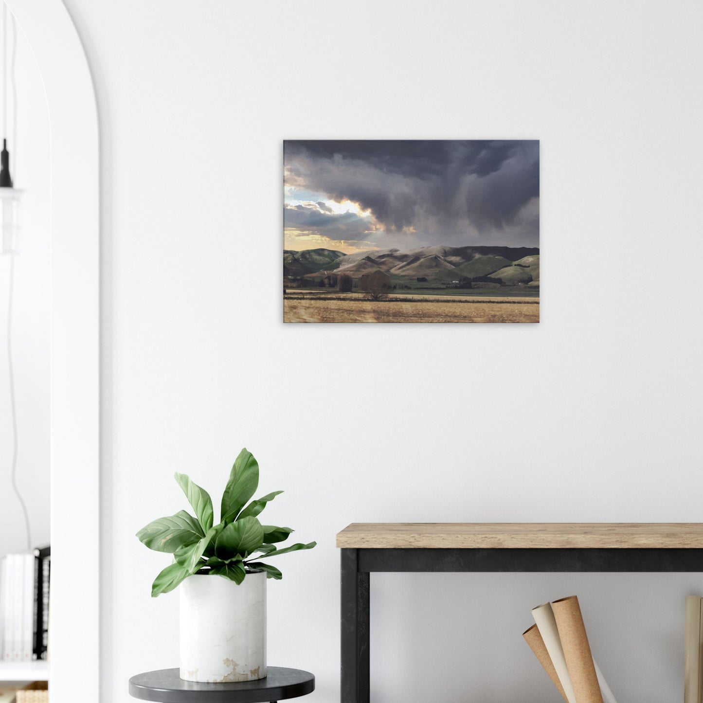 Landscape artwork of Te Hauke hills under dark clouds with beams of light breaking through.