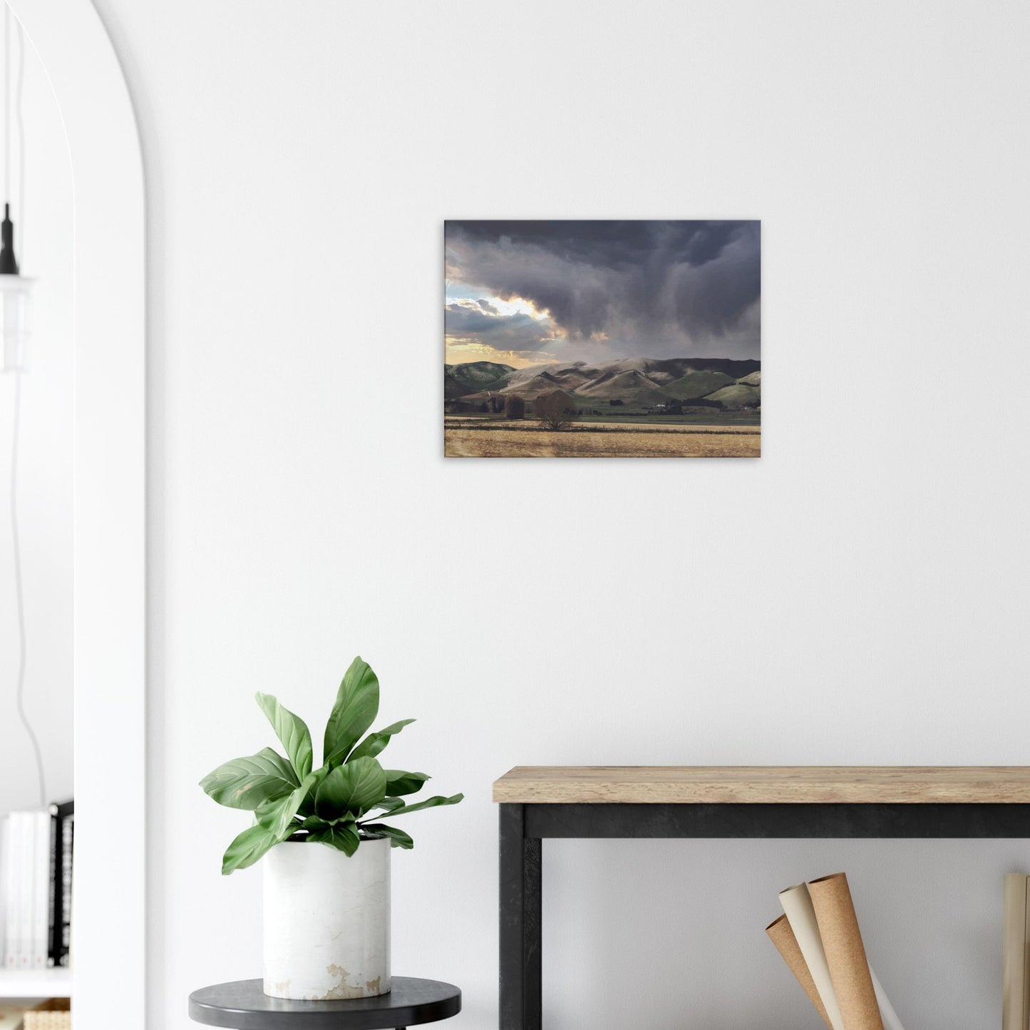 Landscape artwork of Te Hauke hills under dark clouds with beams of light breaking through.