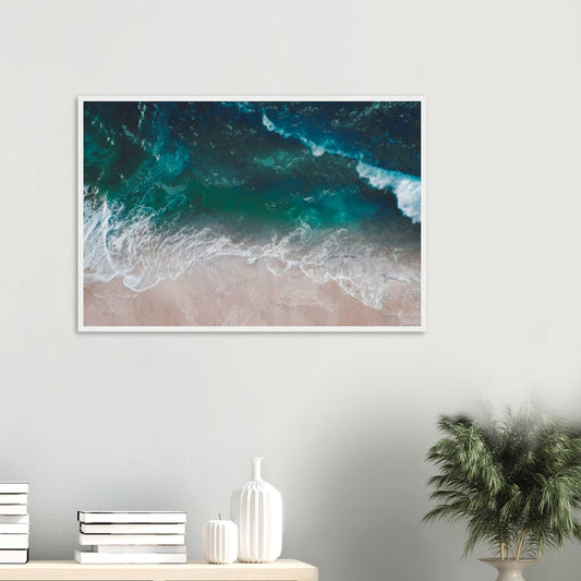 Aerial view of ocean waves rolling onto sand in teal and blue tones.