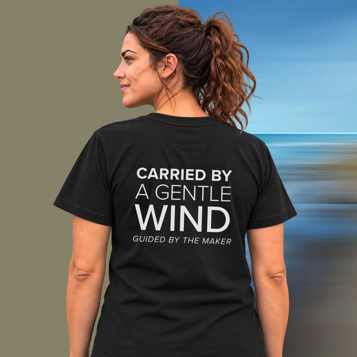 Model wearing the 'Carried by a gentle wind' back print tee in black, large message printed on the back - Blend Designs NZ