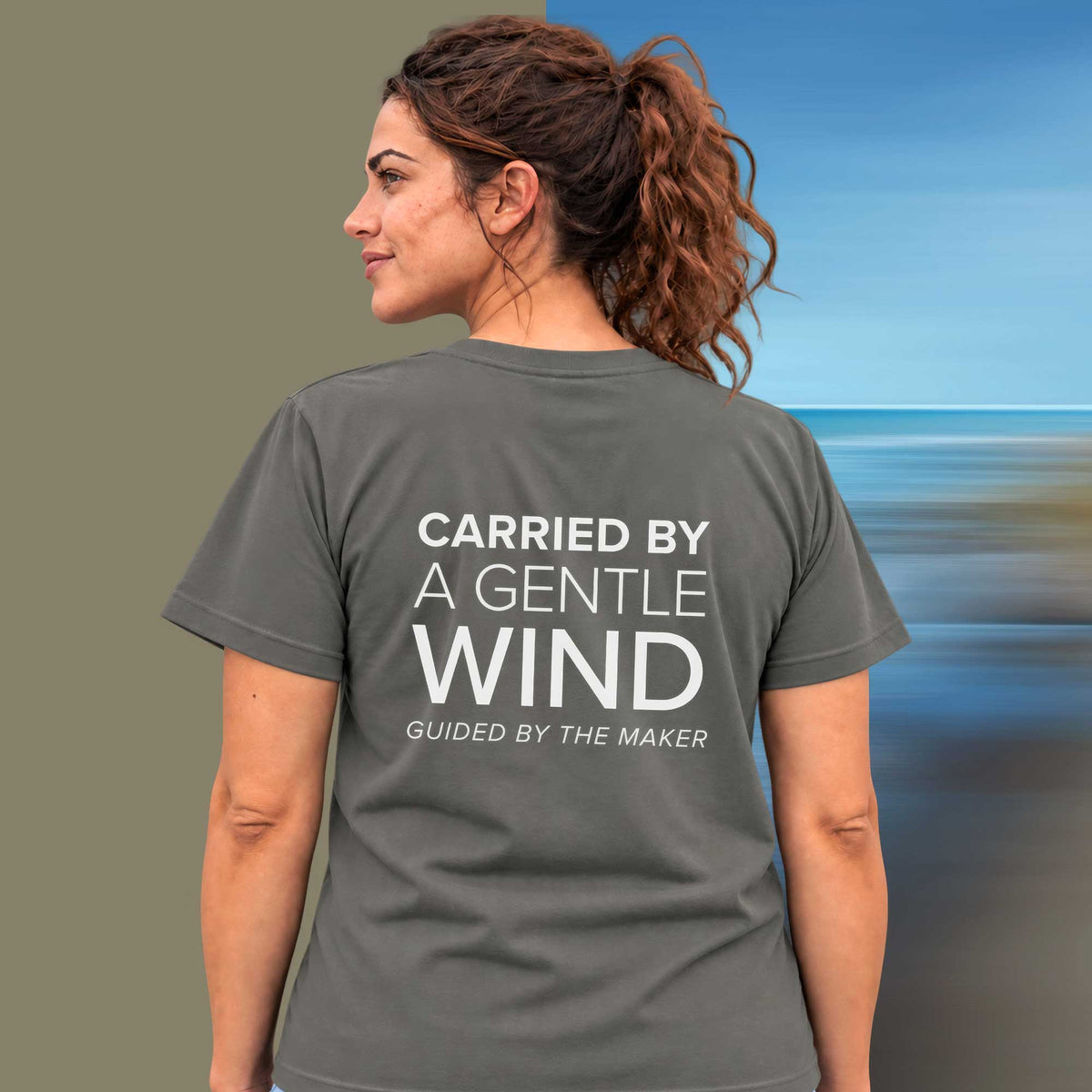 Model wearing the 'Carried by a gentle wind' back print tee in charcoal, large message printed on the back - Blend Designs NZ