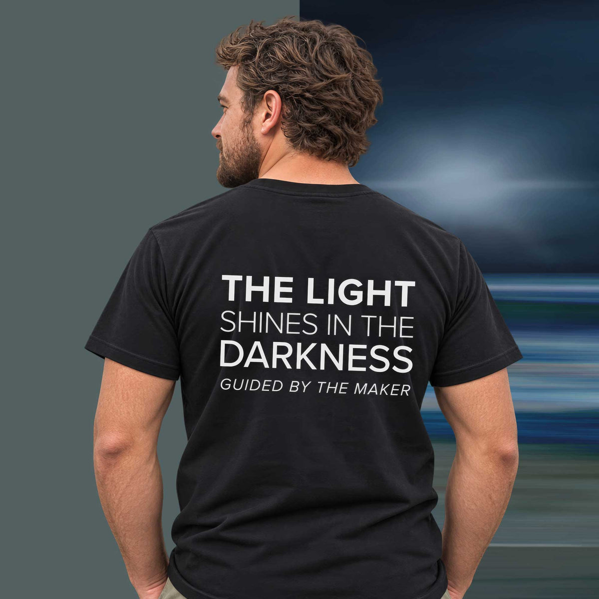 Model wearing the 'The light shines in the darkness' back print tee in black, large message printed on the back - Blend Designs NZ