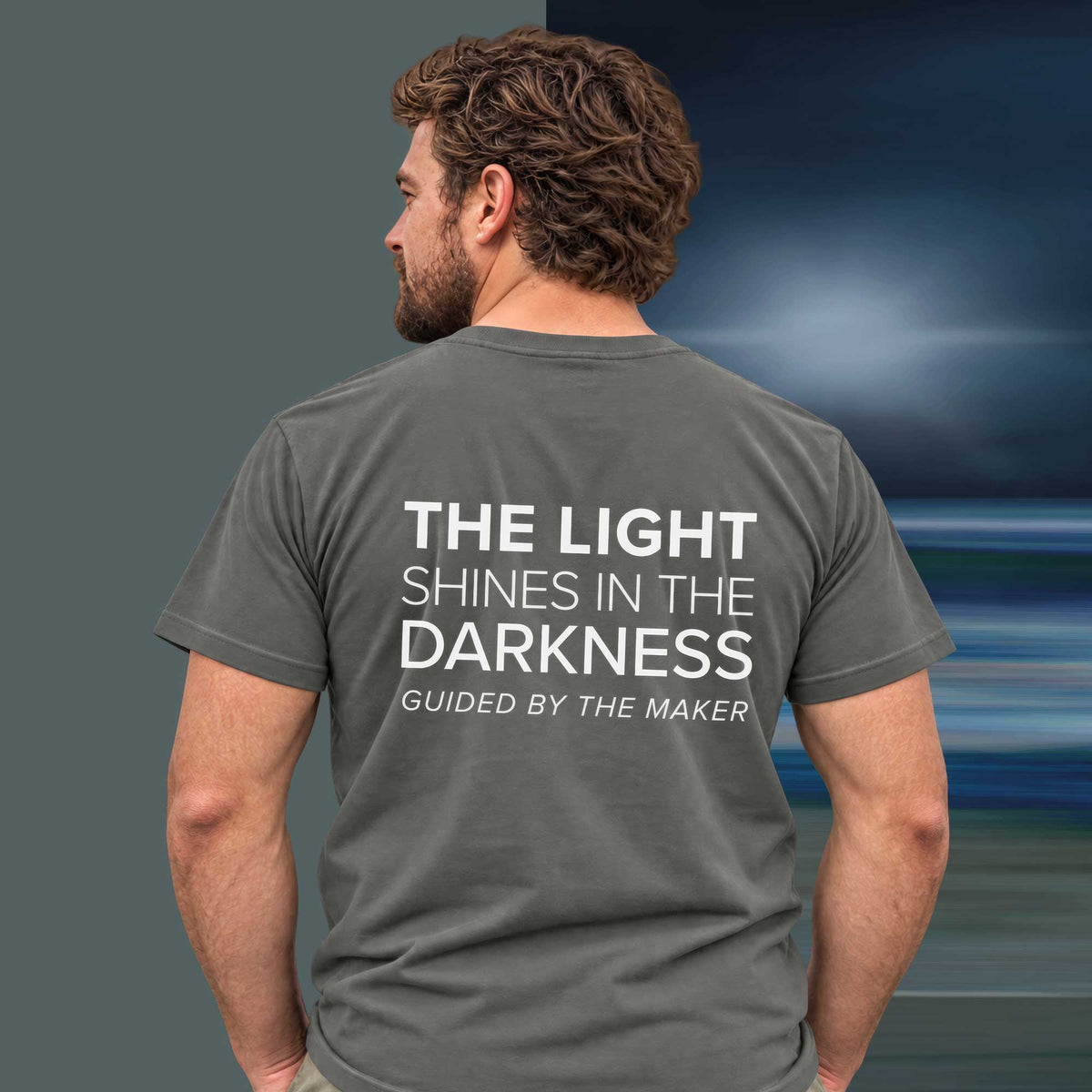 Model wearing the 'The light shines in the darkness' back print tee in charcoal, large message printed on the back - Blend Designs NZ