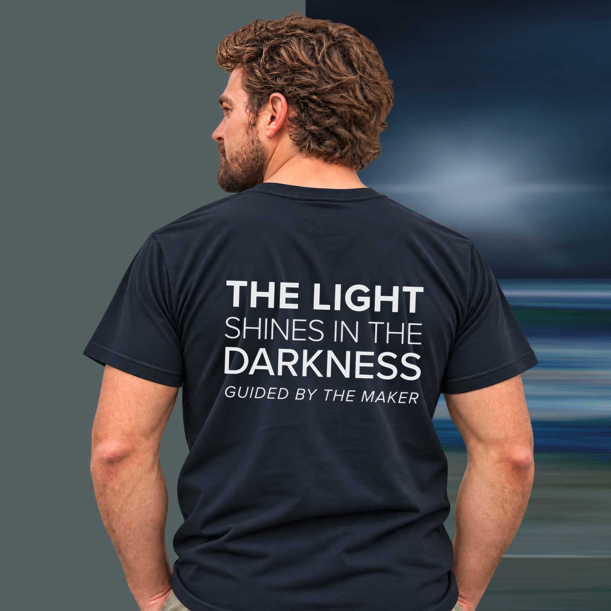 Model wearing the 'The light shines in the darkness' back print tee in navy, large message printed on the back - Blend Designs NZ