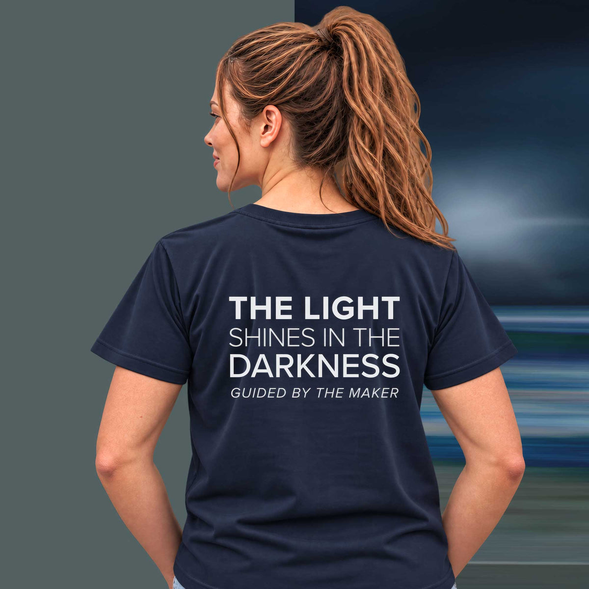 Model wearing the 'The light shines in the darkness' back print tee in navy, large message printed on the back - Blend Designs NZ
