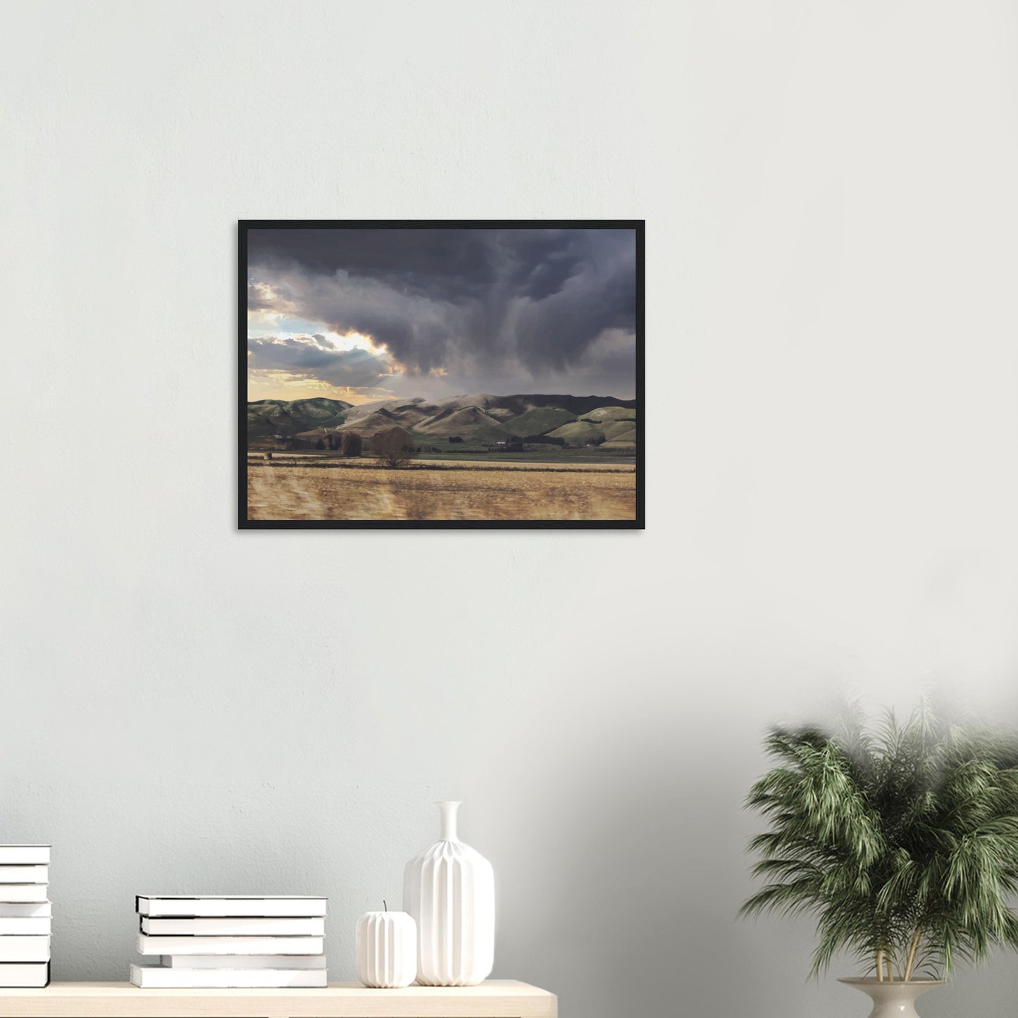 Landscape artwork of Te Hauke hills under dark clouds with beams of light breaking through.