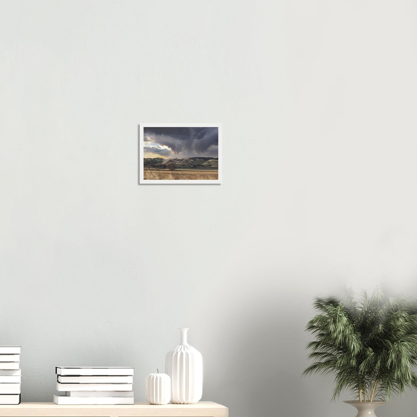 Landscape artwork of Te Hauke hills under dark clouds with beams of light breaking through.