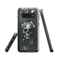 Gothic phone case with a floral skull design in grey tones, featuring white blossoms and dark detailing.