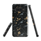 Dark phone case with blackbirds and gold blossoms on black branches.