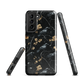 Dark phone case with blackbirds and gold blossoms on black branches.